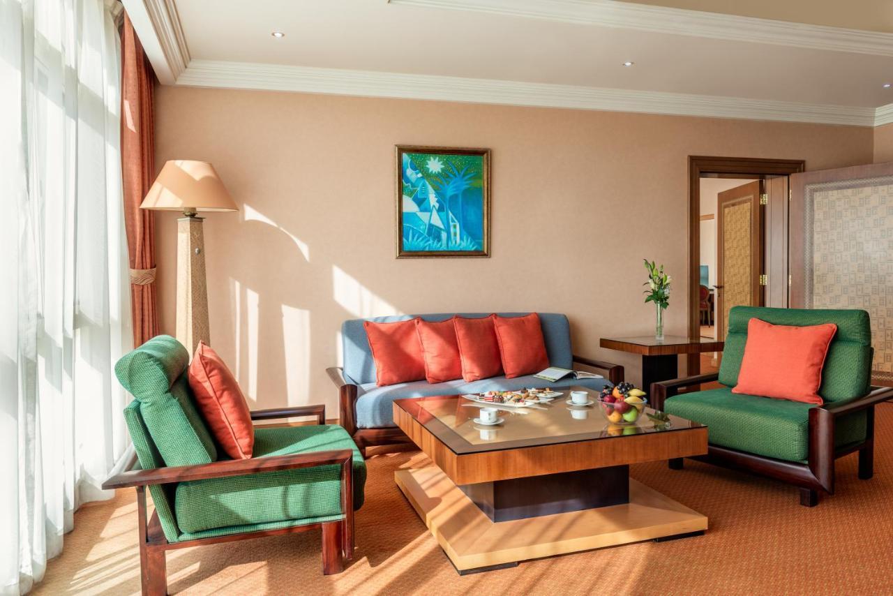 Al Raha Beach Resort & Spa Abu Dhabi Exterior foto The photo shows a cozy living room with a warm ambiance. There are two sofas: one in green with red cushions and another in blue with red cushions, arranged around a wooden coffee table. On the table, there are some fruits and a small decorative item