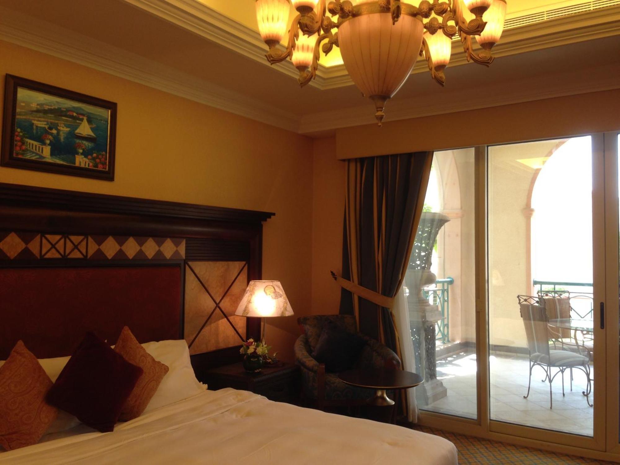 Al Raha Beach Resort & Spa Abu Dhabi Exterior foto The photo shows the interior of a hotel room. The room features a large bed with decorative cushions and a wooden headboard. There's a bedside lamp emitting a warm light, and a painting is hung on the wall above the bed. To the right, there's a windo