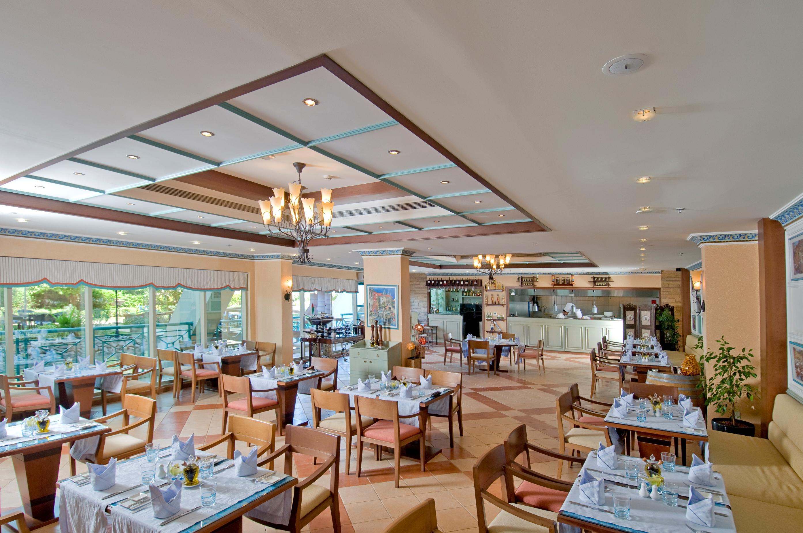 Al Raha Beach Resort & Spa Abu Dhabi Restaurant foto The photo shows the interior of a restaurant. It features a spacious dining area with multiple tables neatly arranged, each set with tableware and cloth napkins. The decor includes a decorative ceiling with lighting fixtures, and large windows that p