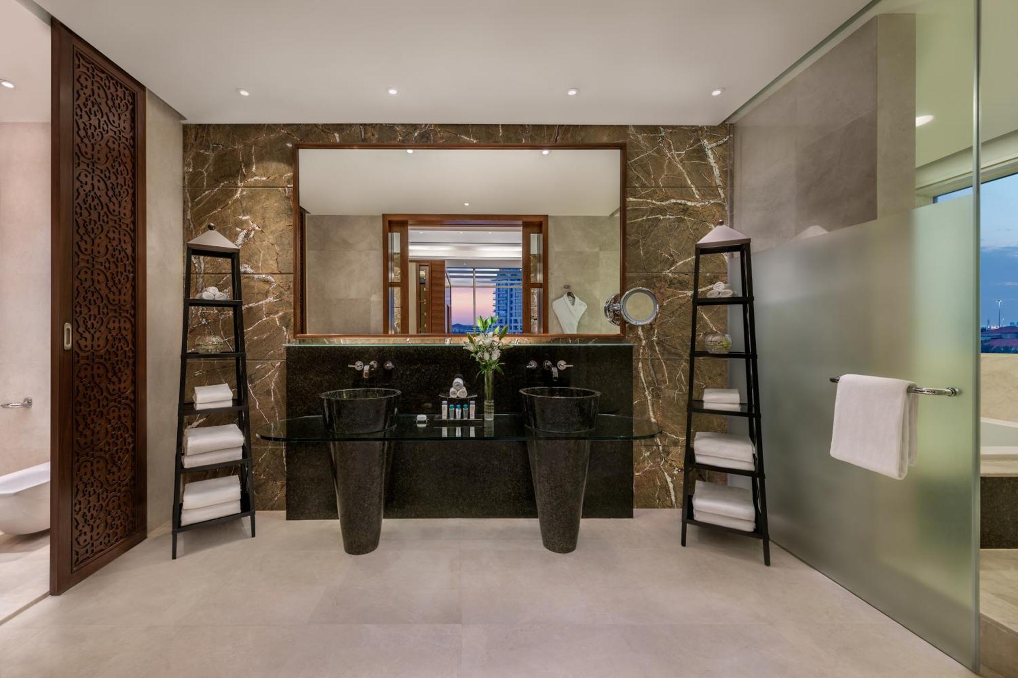Al Raha Beach Resort & Spa Abu Dhabi Exterior foto The photo shows a modern, elegant bathroom interior. It features a large mirror hanging above a double-sink vanity with a dark stone countertop. On either side of the vanity are tall, slender vases that might be holding decorative elements. There are