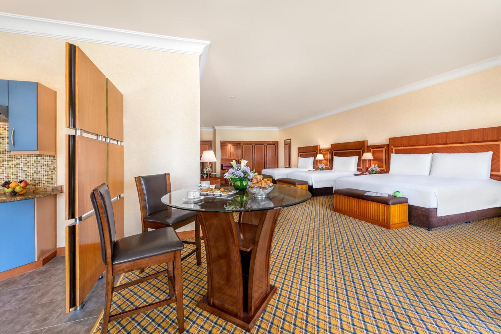 Al Raha Beach Resort & Spa Abu Dhabi Cameră foto The photo displays a spacious hotel room. It features two large beds with white bedding, a circular glass dining table with a decorative floral centerpiece, and a couple of chairs around it. There is a wooden cabinet along one wall, and the room has 